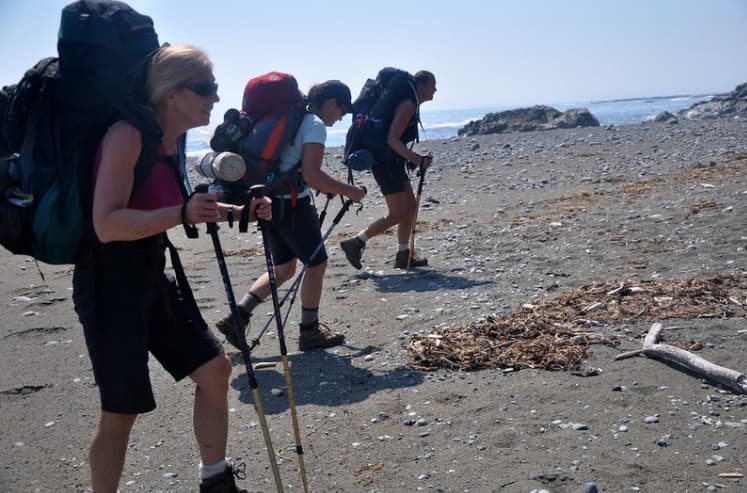 三名背着背包和登山杖的徒步旅行者在中途徒步。